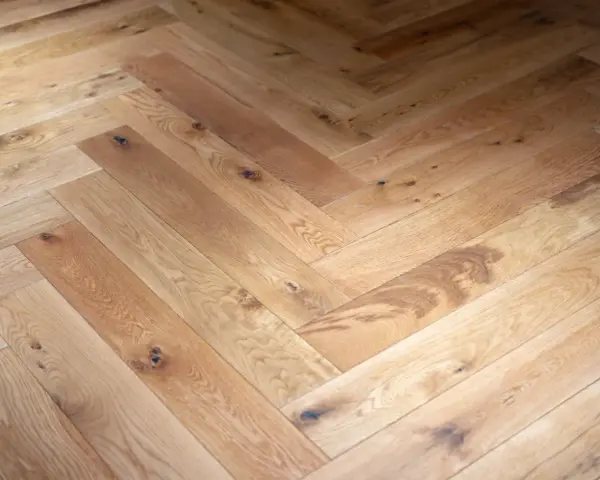 Tarima de madera en espiga, con nudos y vetas naturales, creando un patrón clásico y cálido.