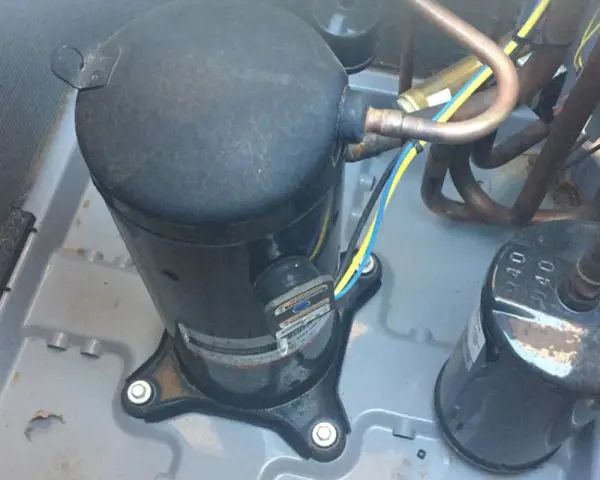 Close-up of an AC pump replacement in progress. A large black compressor sits on a gray base, connected to copper tubing and wires.