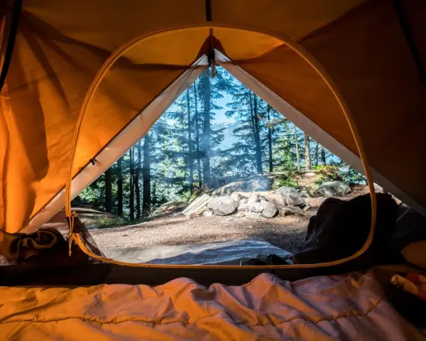 Vue de l'intérieur d'une tente orange, un feu crépite dehors. L'obligation sécurité camping est respectée avec ce campement bien installé.