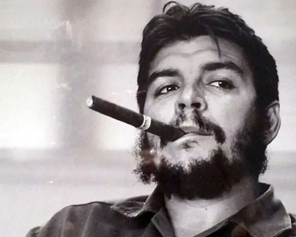 Portrait en noir et blanc de Che Guevara, cigare aux lèvres, regard intense. L'image évoque sa légende, même après sa mort.