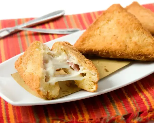 Mozzarella in carrozza dorata e filante, cotta in friggitrice ad aria, servita su un piatto bianco con tovaglietta colorata.