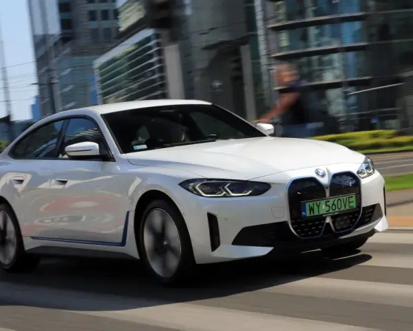 Białe BMW i4 w ruchu miejskim, z widocznymi światłami LED i grillem.