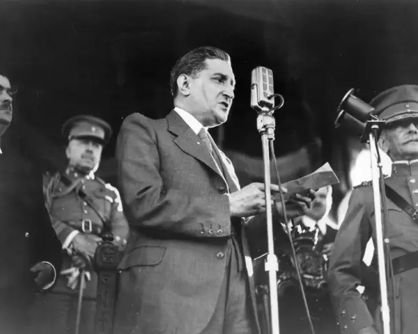 Un homme en costume parle à un microphone, entouré d'officiers en uniforme. Un moment clé de la dictature portugaise de Salazar.