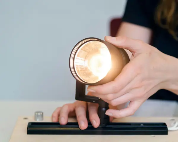 Händer justerar en lampa, kanske för att ta bort dimmer. Ljuset är starkt.