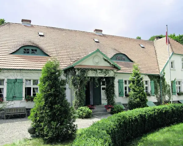 Urokliwy dwór Wybickich z zielonymi okiennicami i pnączami.