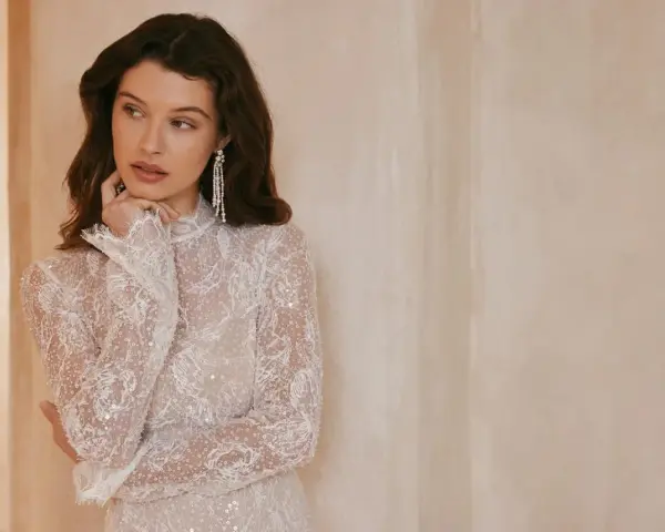 Elegancka, biała sukienka bez dekoltu, zdobiona koronką i cekinami, z długimi rękawami.