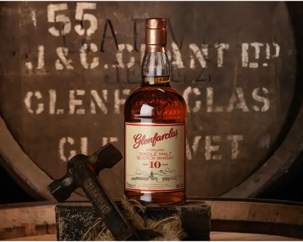 Glenfarclas 10YO, idealny wybór do rankingu top 10 whisky. Butelka na tle beczki z destylarni.