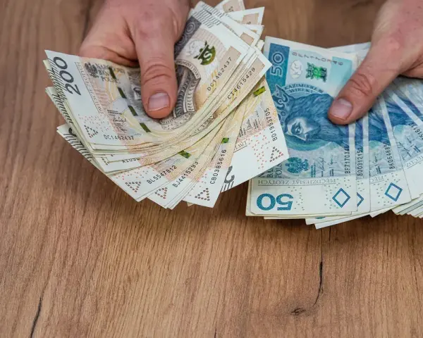 Dłonie trzymające stosy polskich banknotów 200 zł i 50 zł, być może na sześciomiesięczną odprawę emerytalną.