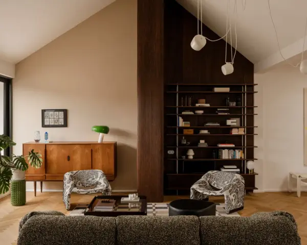 Salón acogedor con **techo inclinado interior**, muebles de madera, estanterías y sillones estampados.