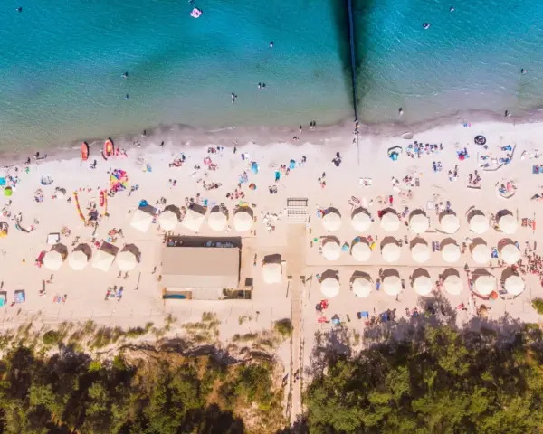 Plaża z parasolami i ludźmi, idealna na wakacje all inclusive Polska.
