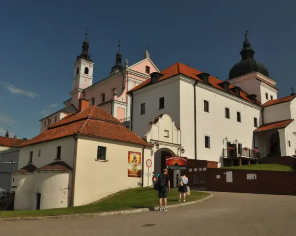 Białe budynki z czerwonymi dachami, wieże i kopuła tworzą malowniczy klasztor kamedułów.