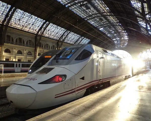 Biały pociąg Renfe, najszybszy pociąg w Europie, stoi na dworcu pod szklanym dachem, oświetlony promieniami słońca.