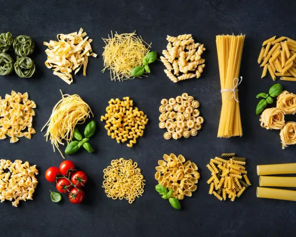 Różnorodne włoskie dania z makaronem: od tagliatelle i spaghetti po farfalle i penne, z dodatkiem pomidorków i bazylii.