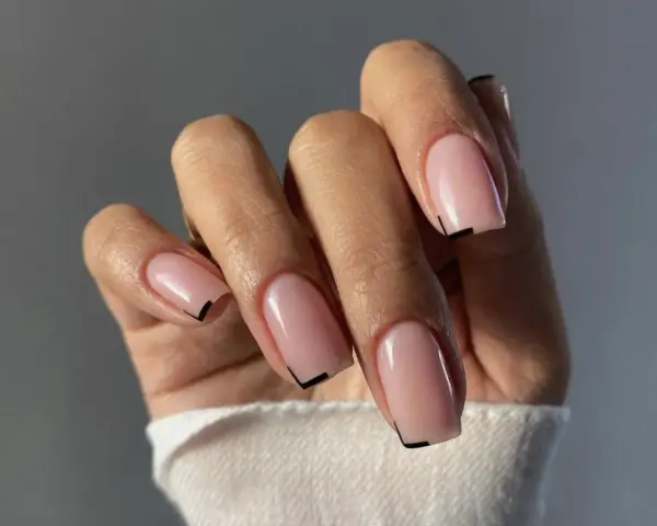 Mano con unghie quadrate naturali, smalto rosa tenue e un sottile dettaglio grafico nero sulla punta.