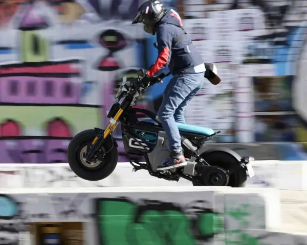 Młody mężczyzna na elektrycznym motocyklu BMW CE02 wykonuje skok na tle kolorowego graffiti.
