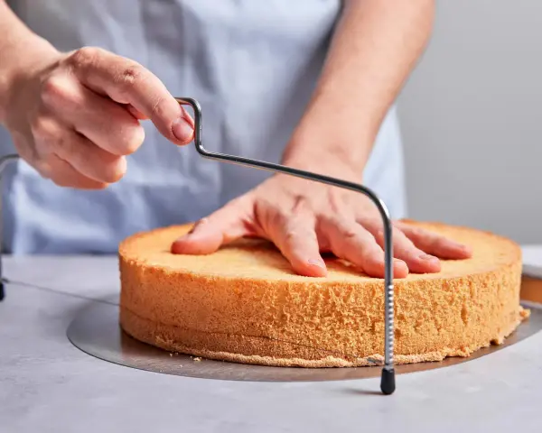 Hände schneiden mit einem Tortenbodenschneider einen Biskuitboden für ein einfaches Cassata Rezept.