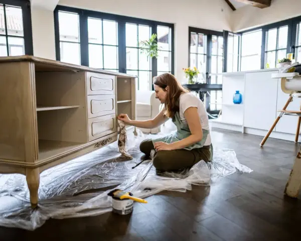 Mujer lijando muebles de madera antiguos para restaurarlos.