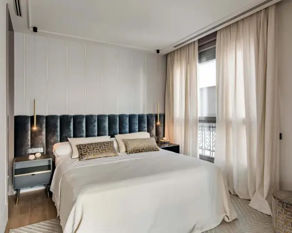 Acogedora habitación pequeña con cama grande, cabecero tapizado, mesitas de noche modernas y cortinas elegantes.