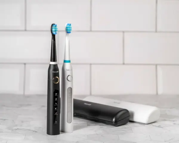 Dwa eleganckie modele szczoteczek sonicznych, czarny i srebrny, z różnymi końcówkami do wyboru. Obok etui podróżne.