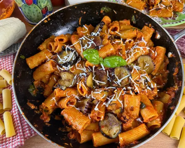 Rigatoni ricchi di melanzane fritte e pomodoro, conditi con ricotta salata grattugiata e basilico fresco. Un piatto di pasta alla norma invitante.