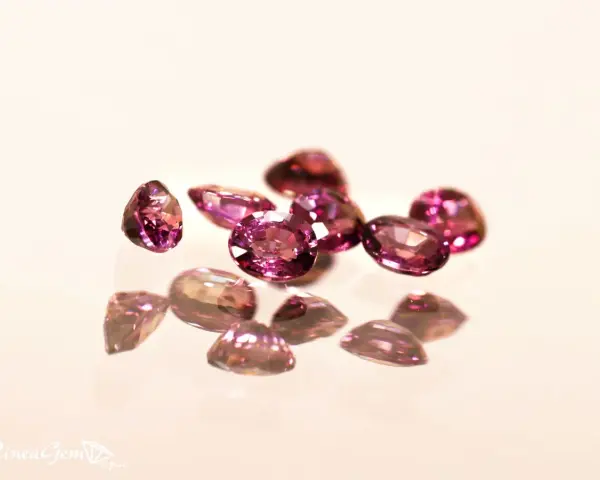 Un gruppo di pietre di granato rosa sfaccettate, che riflettono la luce su una superficie lucida.