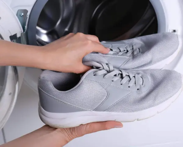Ręce wkładają szare adidasy do pralki. Dowiedz się, jak prać adidasy w pralce, aby odświeżyć swoje ulubione buty.