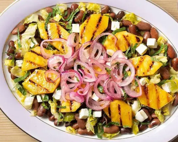 Ensalada de frijoles, piña a la parrilla, queso y cebolla morada en un plato blanco.
