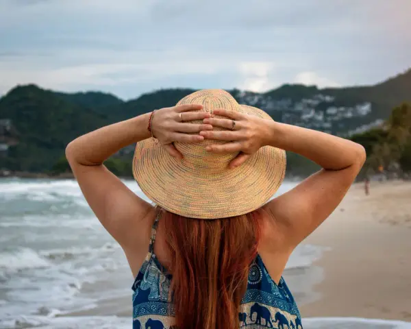 Frauenhände halten Hut am Strand. Endlich Zeit für Urlaub, der gesetzliche Urlaubsanspruch ab 50 ist wohlverdient.
