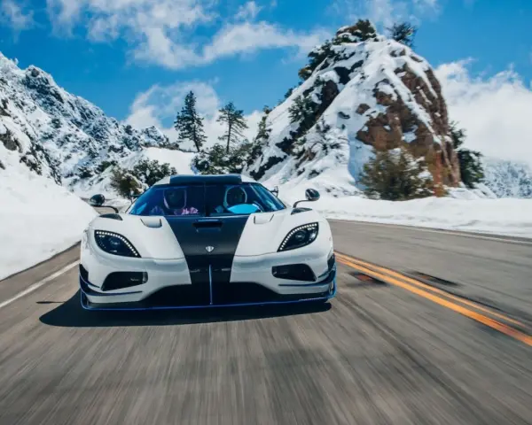 Biały Koenigsegg Agera RS z czarnym pasem na masce pędzi po ośnieżonej górskiej drodze.