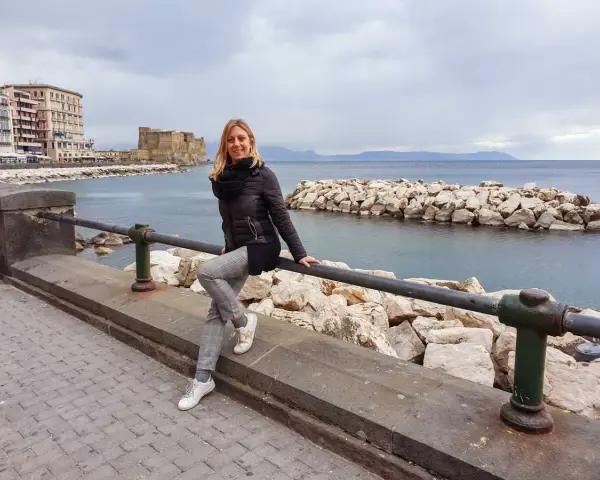 Woman sitting on a railing with Castel dell'Ovo and the sea in the background in Naples.