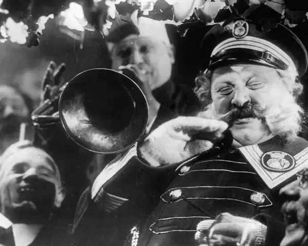 Un uomo con baffi e barba folta suona una tromba, circondato da volti sorridenti. Un'atmosfera da kammerspiel, un dramma intimo e intenso.