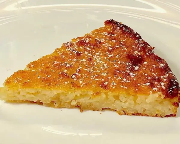 Una fetta di torta di riso, profumata e dorata, come la torta di riso ricetta della nonna, spolverata di zucchero a velo.