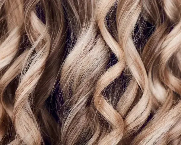Falujące, blond włosy z subtelnymi refleksami, które mienią się w świetle, tworząc efekt głębi.