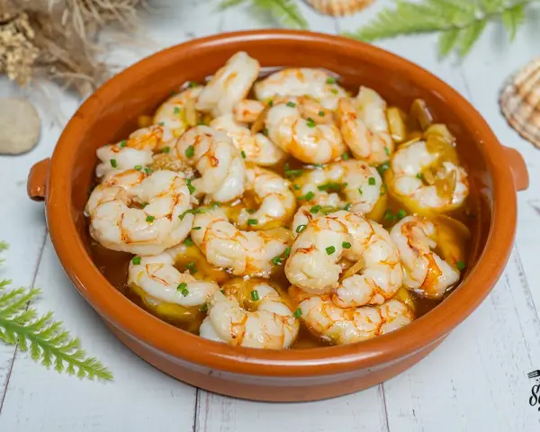 Gambas al ajillo burbujeantes en cazuela de barro, con perejil picado y un toque de aceite de oliva. ¡Un clásico irresistible!