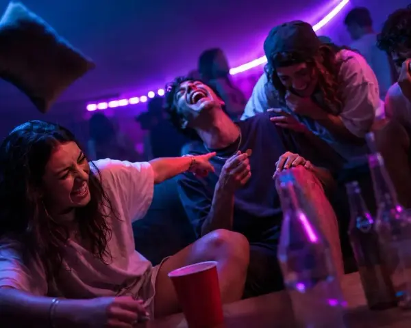 Ungdomar skrattar och har kul på en fest, kanske med kluriga gåtor till festen. Ljusen är lila och blå.
