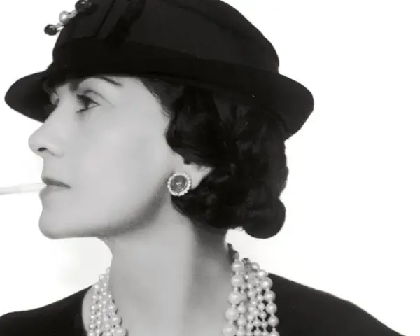 Coco Chanel, con sigaretta e perle, icona di stile, ci ricorda dove è nata Coco Chanel, un'ispirazione senza tempo.