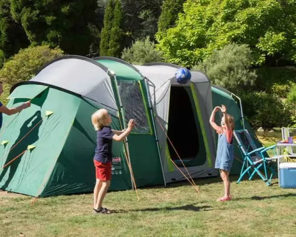 Radosny camping rodzinny: tata rozkłada namiot, dzieci bawią się piłką, mama przygotowuje posiłek.