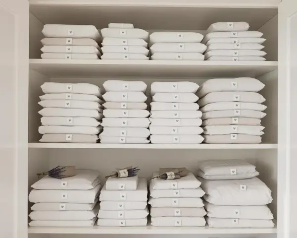 Étagères remplies de linge de lit blanc et beige plié. Une astuce rangement linge de lit pour une organisation parfaite.