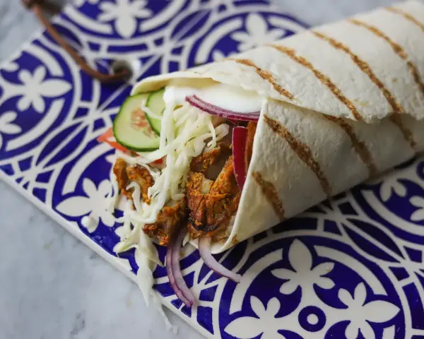 Pyszny kebab w picie z soczystym mięsem, chrupiącą kapustą, pomidorem, ogórkiem i czerwoną cebulą, podany na ozdobnym talerzu.
