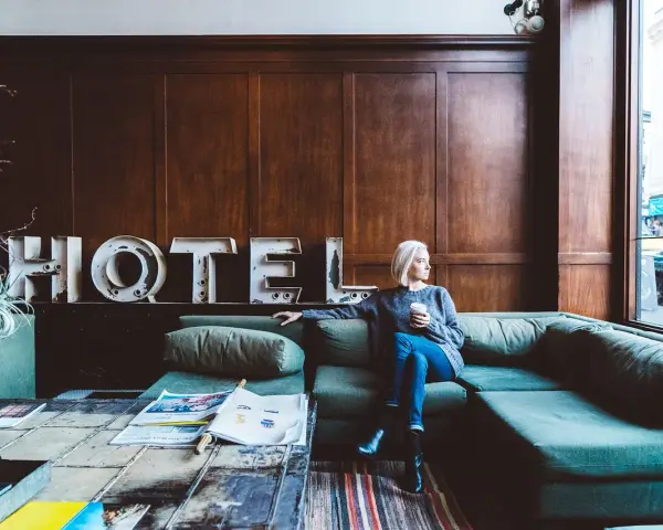 Kobieta z kawą siedzi na kanapie w hotelu. Zastanawia się, ile zarabia technik hotelarstwa.