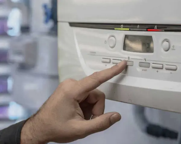 Mano presionando un botón en la caldera de gas, indicando posibles problemas. La pantalla muestra "02".