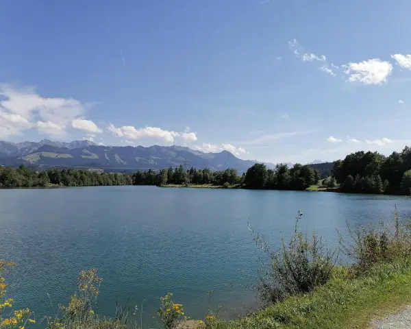 Blauer Himmel über dem Sonthofener See, umgeben von grünen Bäumen und majestätischen Bergen.