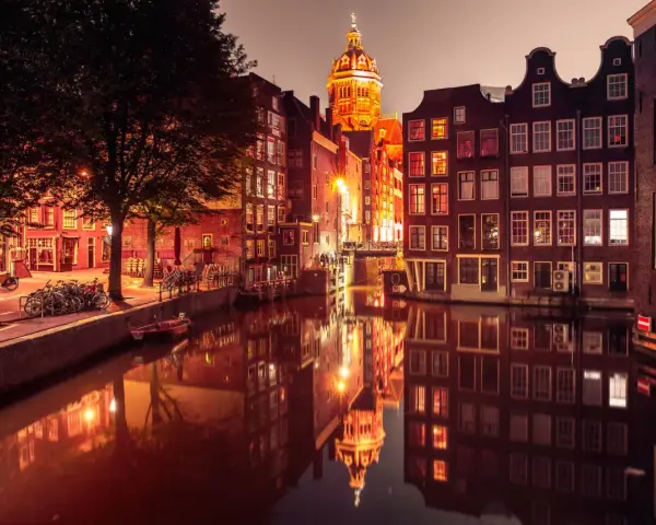 Nocny Amsterdam, kanał odbija oświetlone kamienice i kopułę kościoła. Czerwona ulica Amsterdam w blasku latarni.
