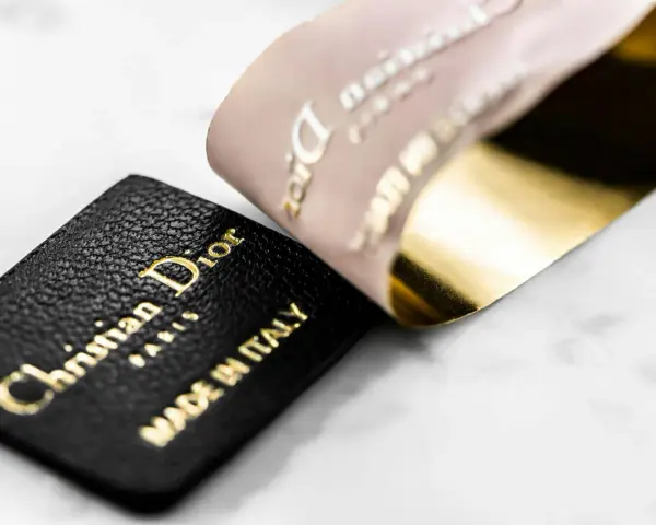 Etichetta in pelle nera con logo Christian Dior Paris e "Made in Italy" dorato, accanto a un nastro Dior francese con finitura oro lucido.