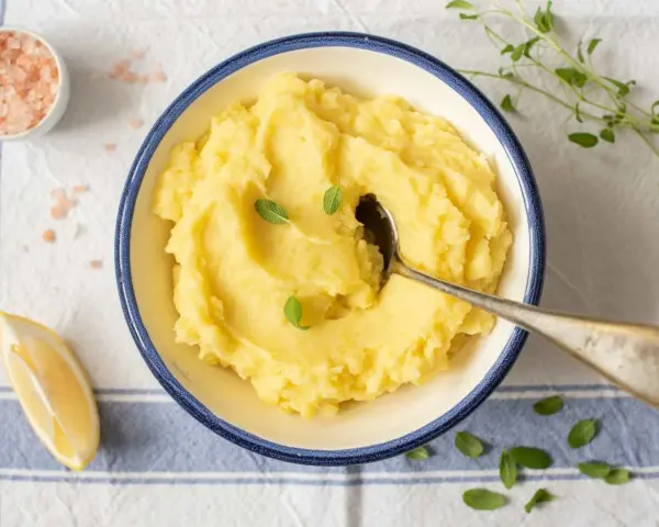 Un cremoso puré de patata de la abuela, servido en un cuenco azul, con una cuchara, limón y sal rosa.