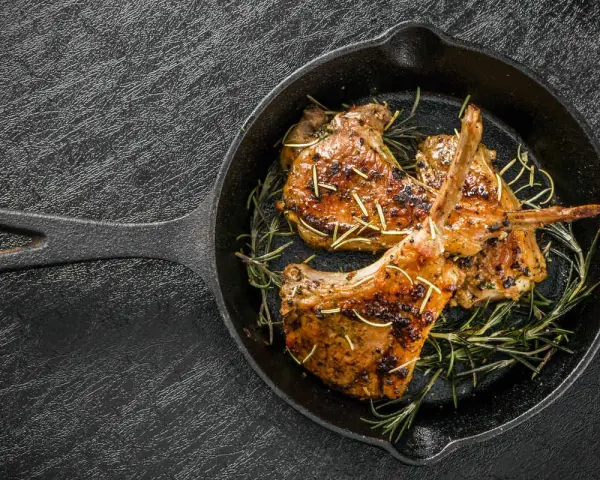 Tre succulenti costolette di agnello in padella, guarnite con rosmarino fresco, pronte per essere gustate.