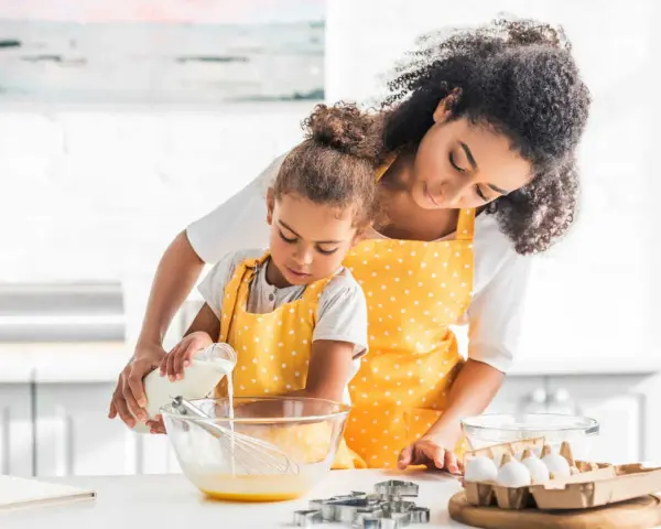 Une mère et sa fille préparent une recette, la petite verse du lait ribot dans un bol.