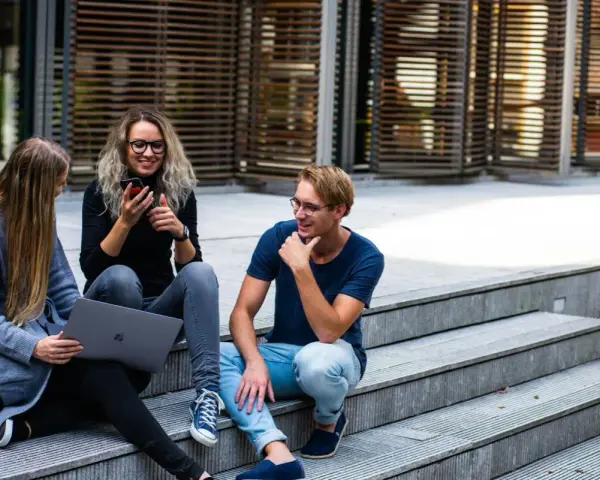 Trójka studentów, w tym jedna osoba na studiach lingwistycznych, siedzi na schodach, korzystając z laptopa i telefonu.