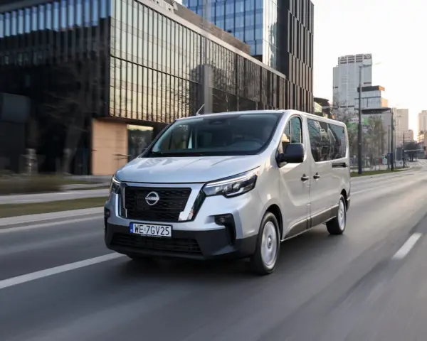 Srebrny van Nissan, jeden z najnowszych nissan modele, jedzie ulicą w nowoczesnym mieście.