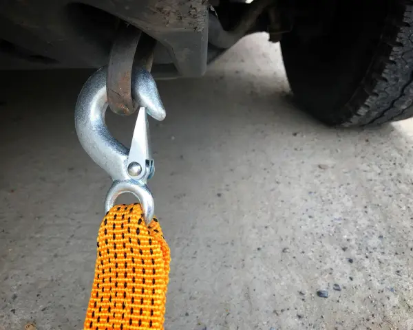 Gancio metallico agganciato al telaio di un'auto, pronto per iniziare a come trainare una macchina. La cinghia arancione è visibile.